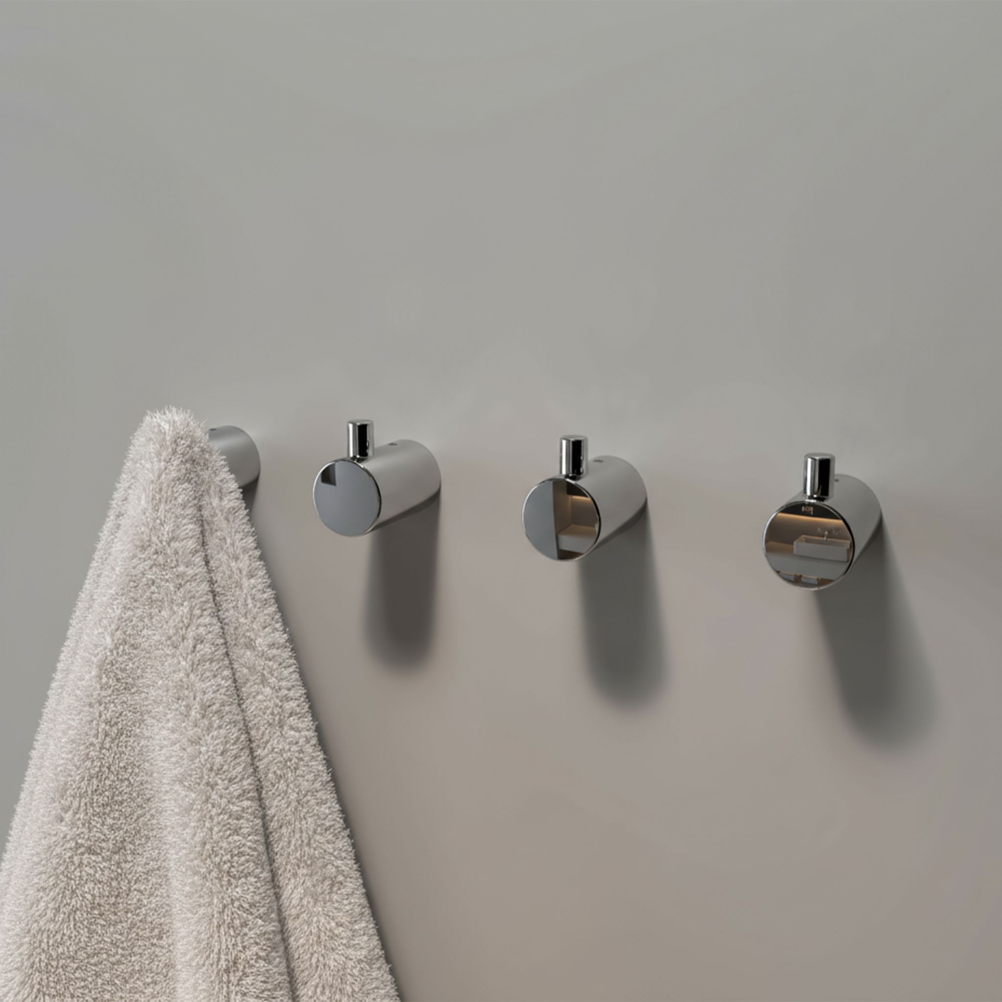 Polished stainless steel round wall hooks mounted in a row on a bathroom wall, with one hook holding a towel